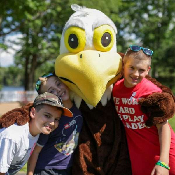 Zeagle the Eagle with arms around two happy campers