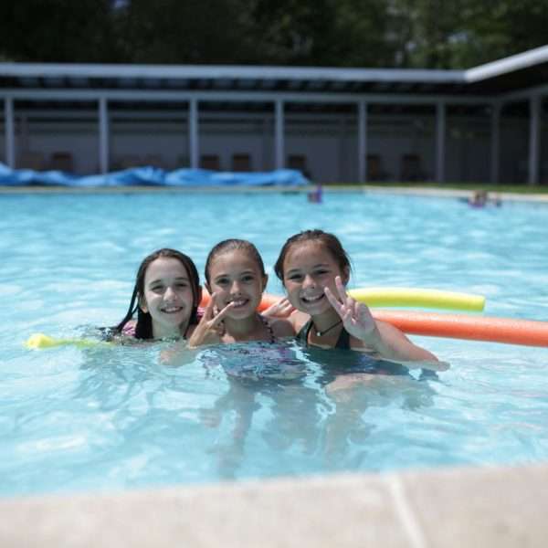 Three female campers with pool noodles smiling into camera