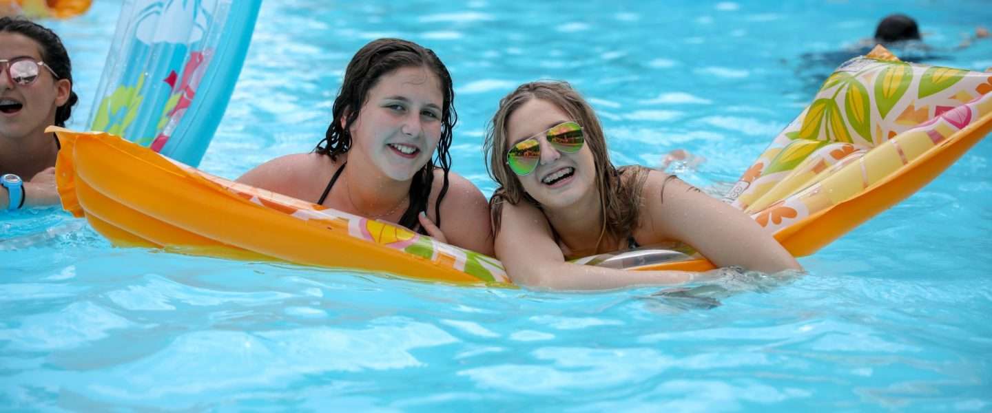 Two female campers floating on a lilo in the pool