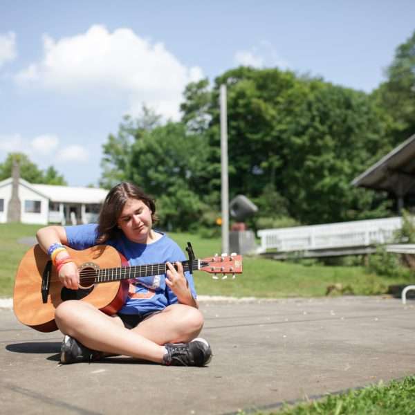 Female camper sitting outside playing guitar