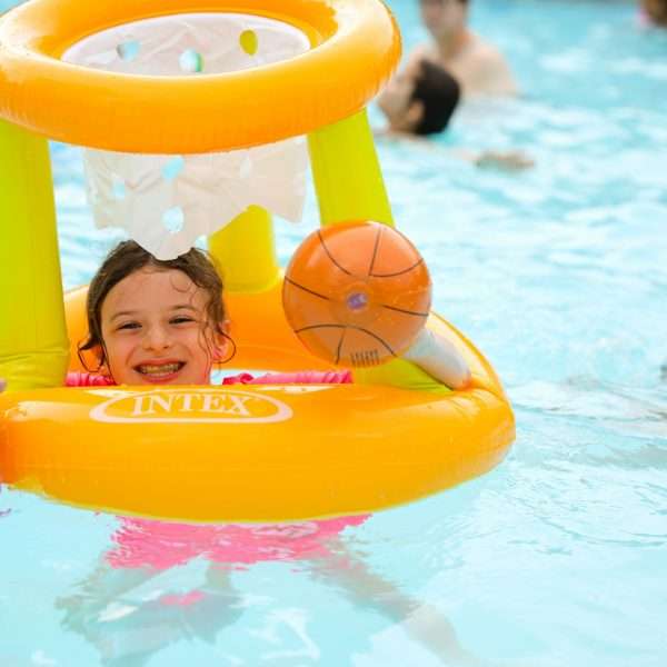 Female camper with inflatable basketball net and ball in the heated pool
