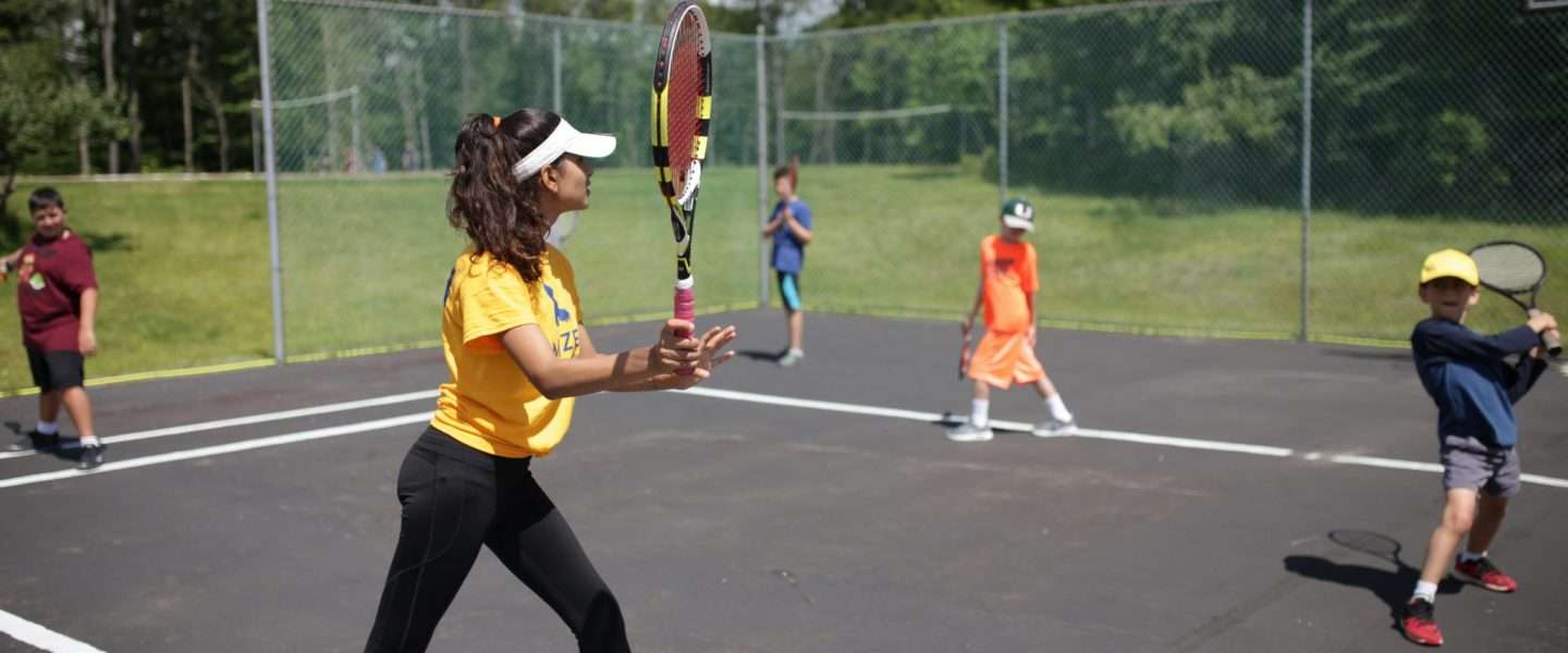 One of the camp counselors playing tennis with campers