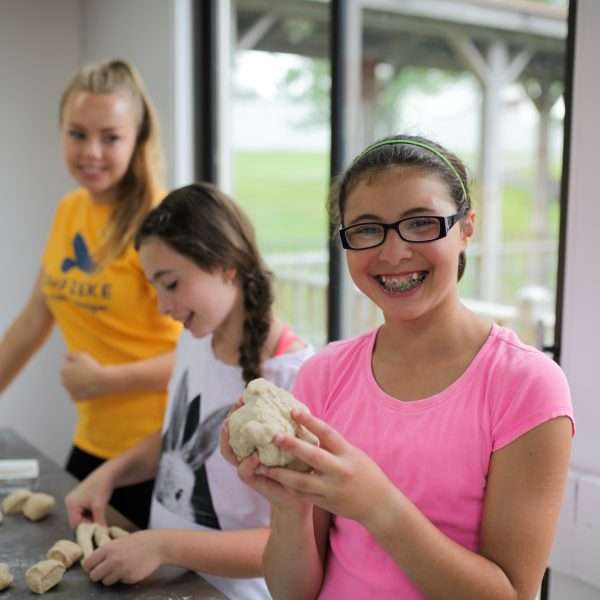 Two female campers kneading dough supervised by a counselor