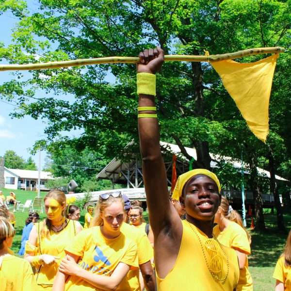 Camp staff all in yellow following one staff member who holds aloft a flag