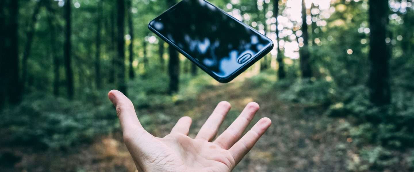 Hand throwing a smartphone into the forest